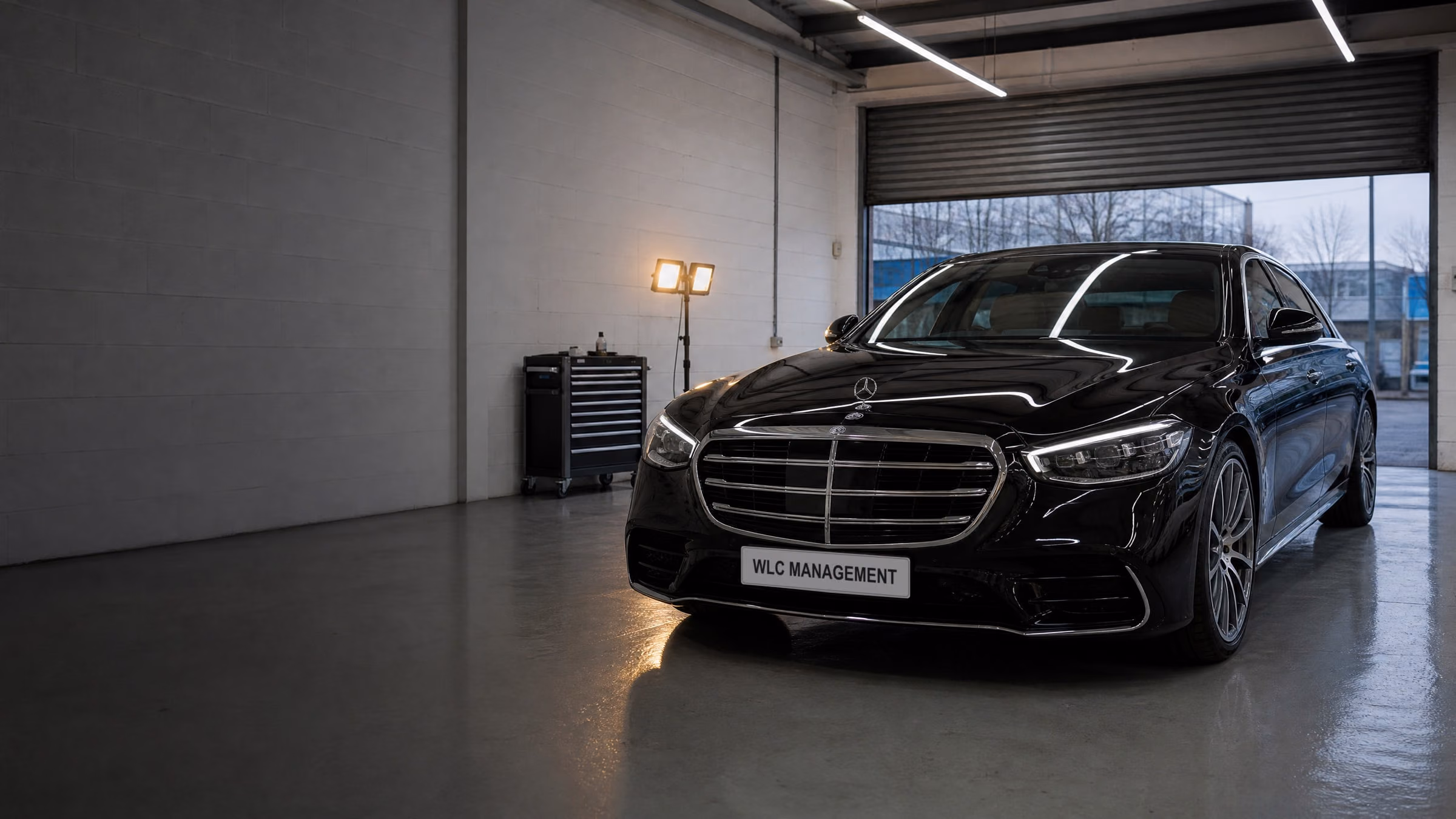 Polished black Mercedes in the workshop, lights reflected along the bonnet