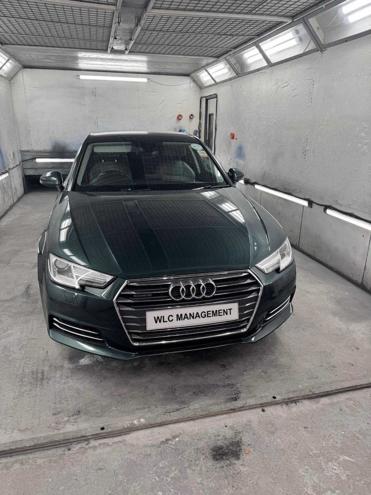 Dark green Audi A4 inside the white spray booth, front view