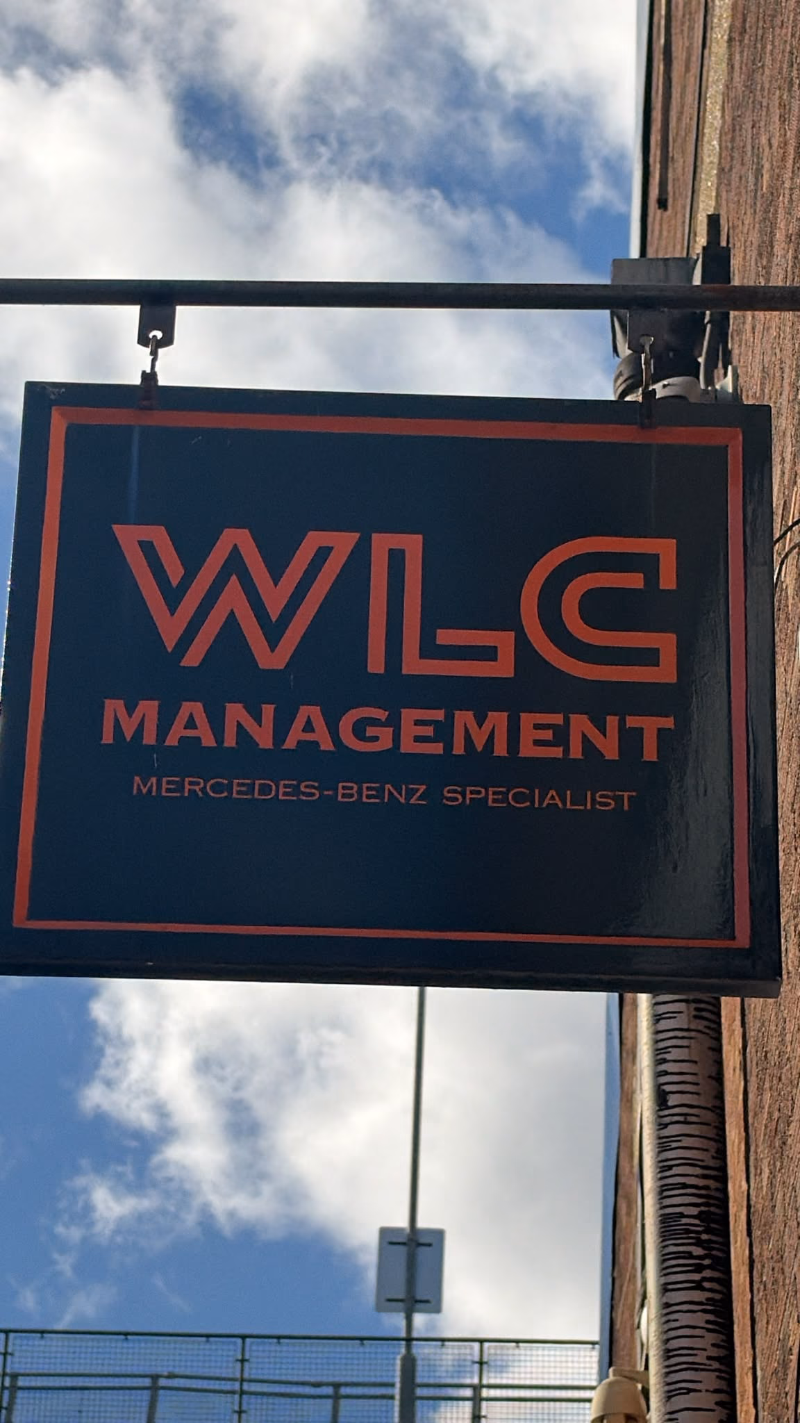 The workshop sign, navy with a red frame: WLC Management, Mercedes-Benz specialist, hanging on the brick wall